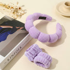 Purple fuzzy neck pillow and slippers on a beige surface with a book and decorative elements.